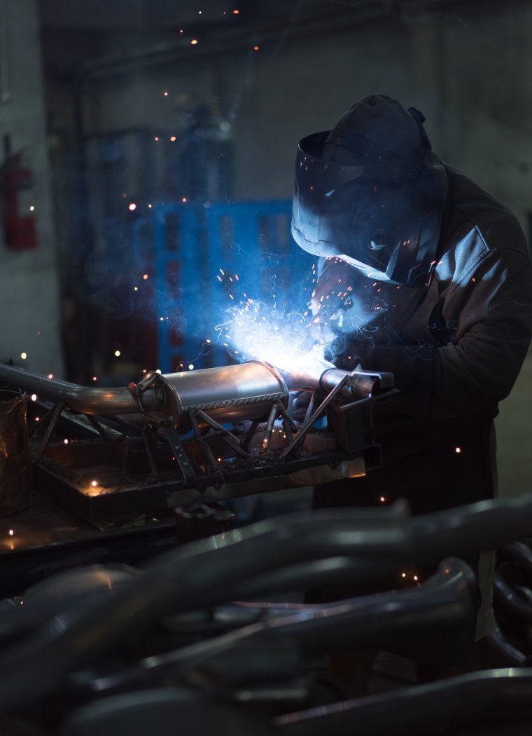 worker-welding-exhaust-pipes-pieces-together.jpg